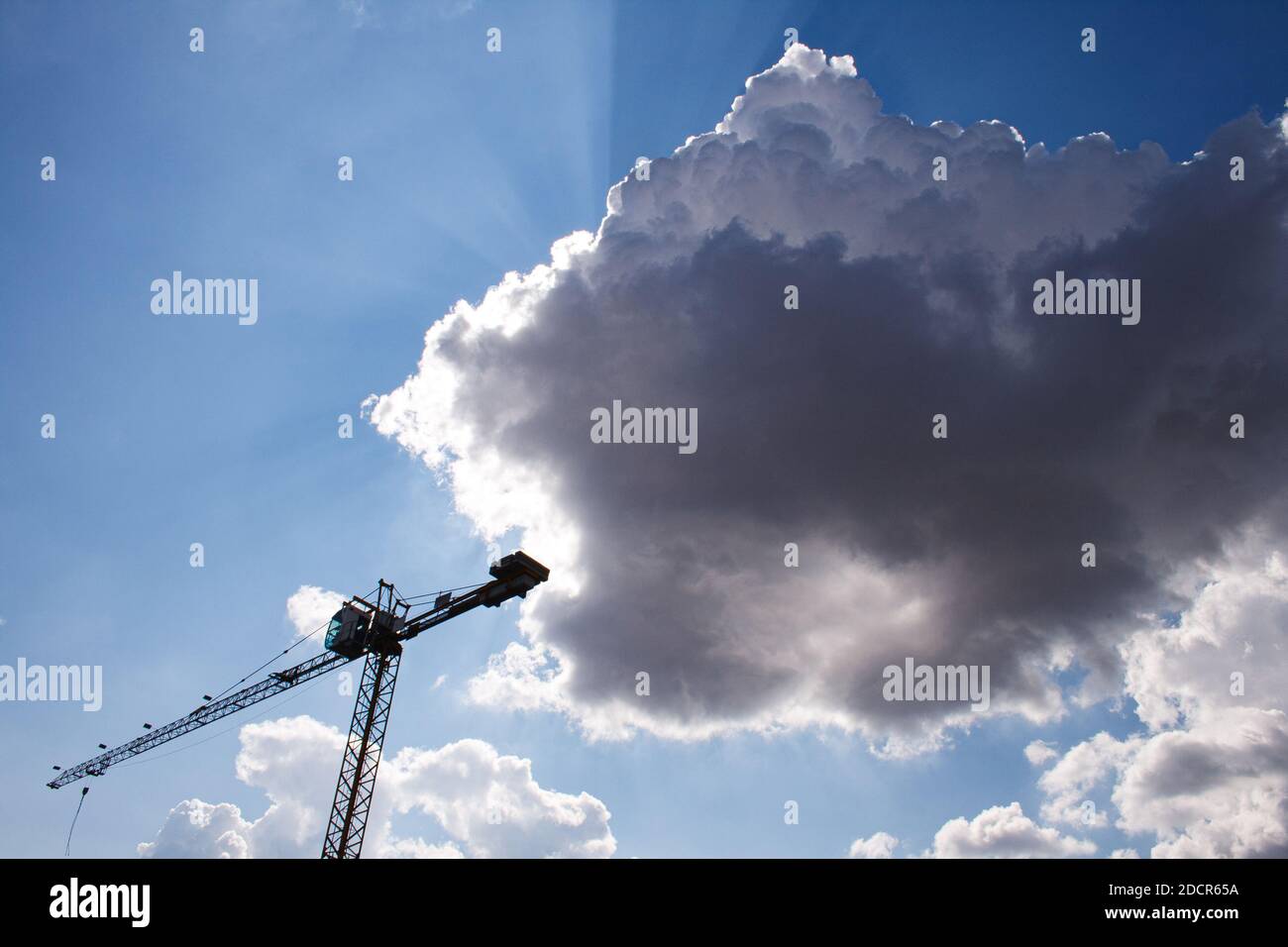 Construction crane on a cloudy sky. The sun is coming out of the clouds Stock Photo