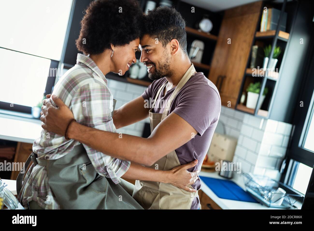 Beautiful couple are hugging and smiling while spending time in kitchen ...