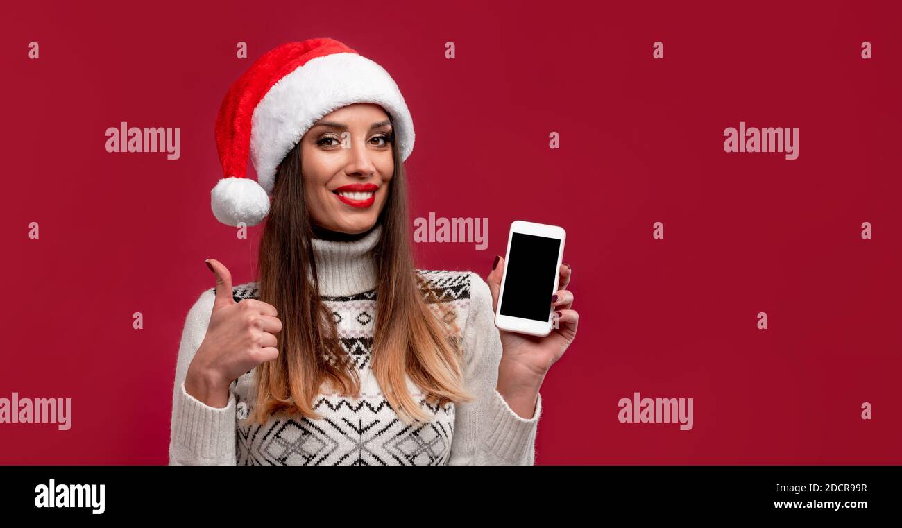 Close up portrait beautifiul caucasian woman in red Santa hat on red studio background. Christmas New Year holiday concept. Cute girl teeth smiling po Stock Photo