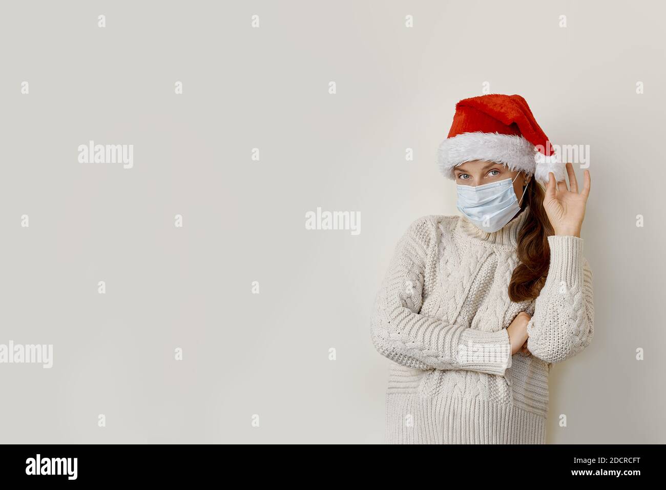 Woman wearing mask and santa hat standing over isolated beige background Stock Photo