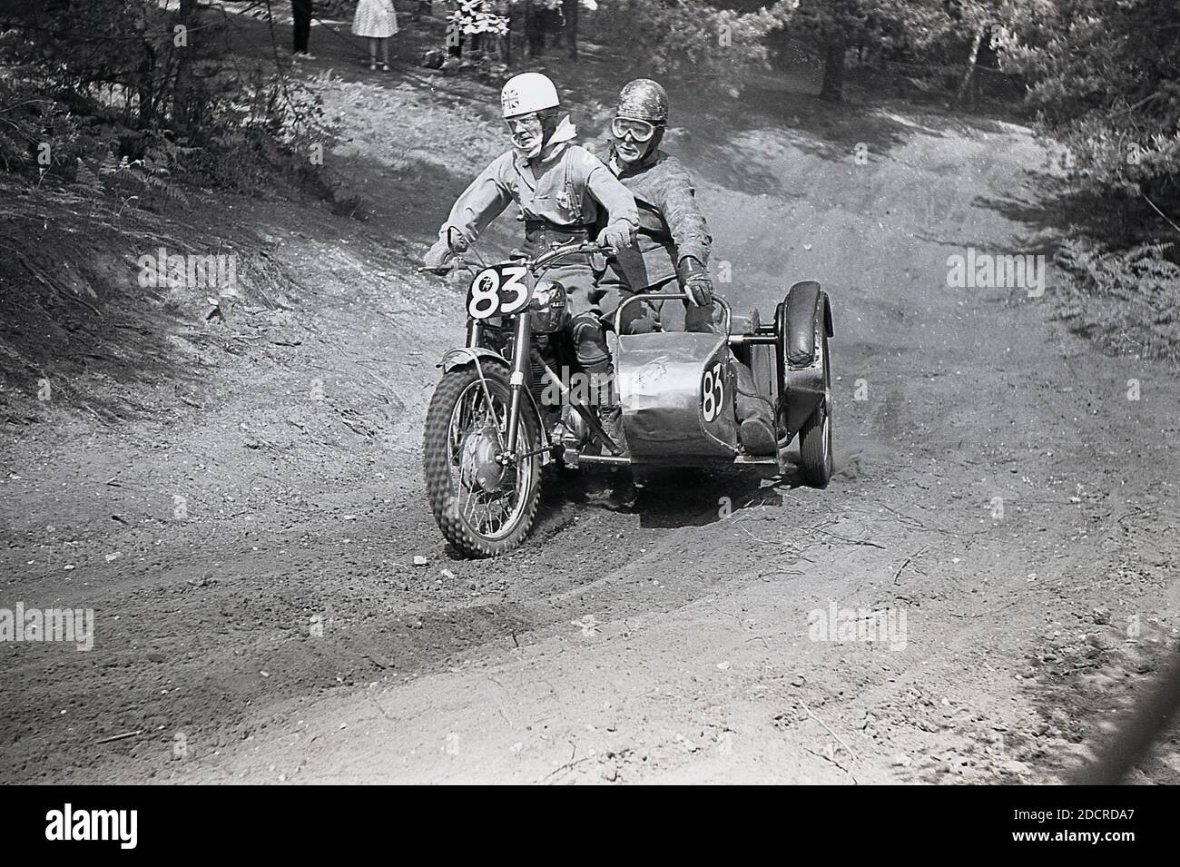 Late 1950s, a male competitor in a motorcycle scrambling event, riding across a muddy trail. Invented in 1924, in Camberley, Surrey, England, the bikes used to scramble in '50s and early '60s were little different from the road bikes of the time, with very little suspension. Today the sport is known as motocross – the French name for cross-country motorcycling – and referred to as Supercross in the USA. Stock Photo