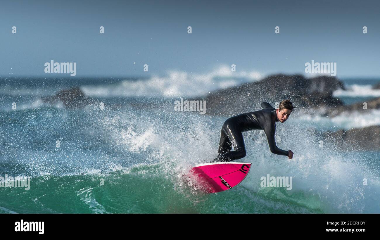 A panoramic image of spectacular surfing action as a young male surfer rides a wave at Fistral in Newquay in Cornwall. Stock Photo
