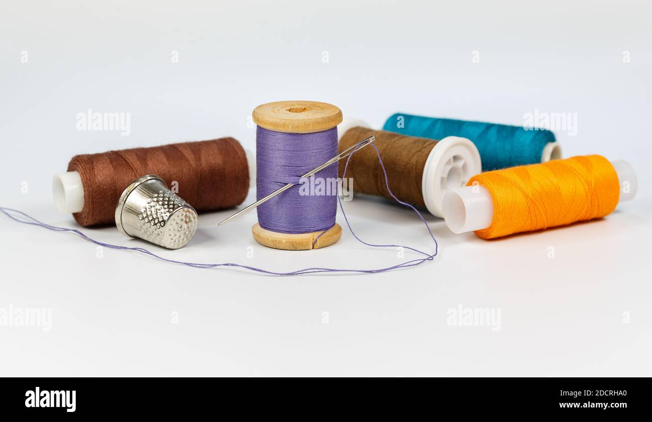 Multicolored thread, needle and thimble on a white background closeup Stock Photo
