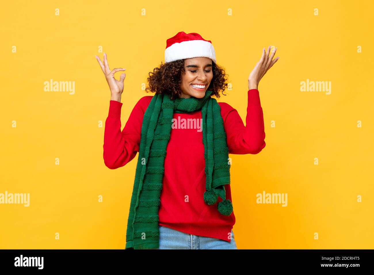 Surprised happy woman in Christmas attire smiling and raising hands up in yellow studio isolated background Stock Photo