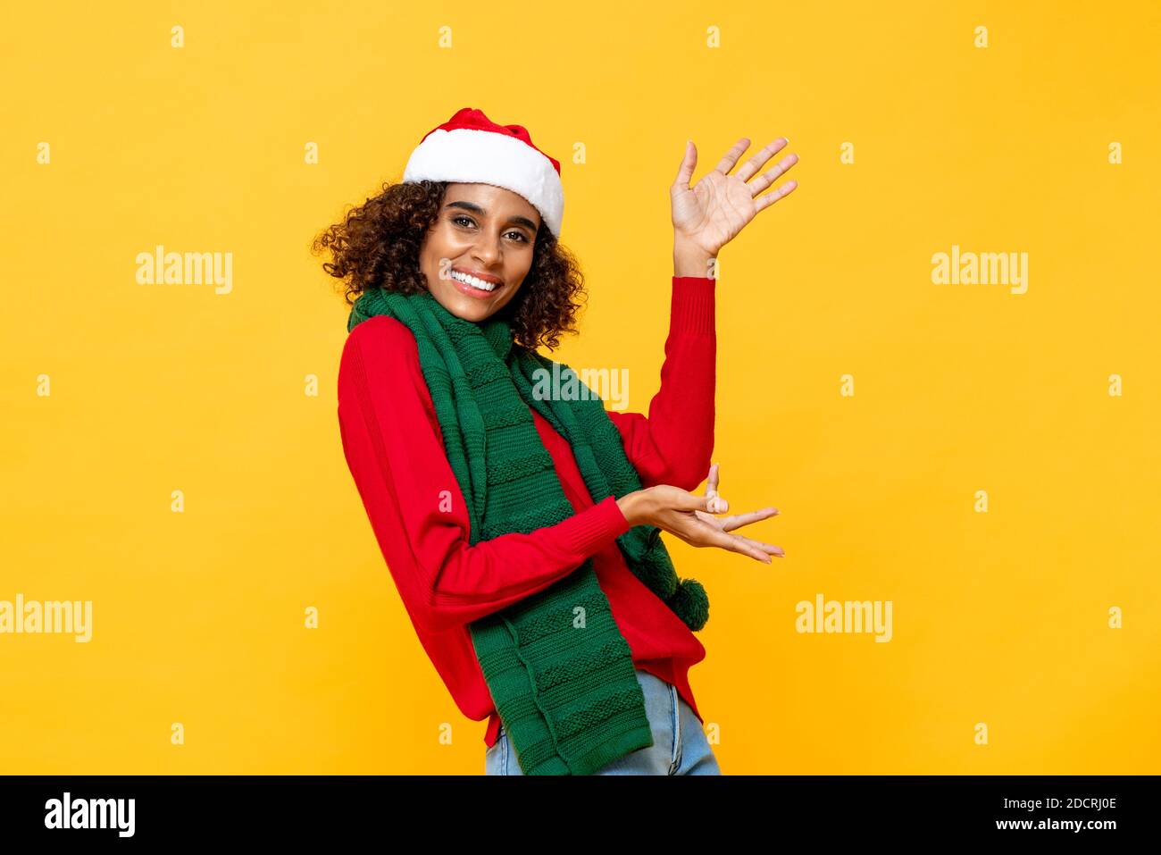 Cheerful happy woman in Christmas attire smiling and raising hands up in yellow studio isolated background Stock Photo