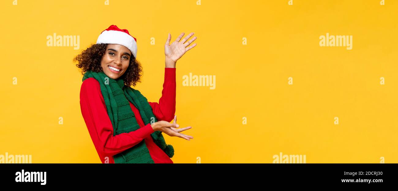 Cheerful happy woman in Christmas attire smiling and raising hands up to copy space in yellow banner isolated background Stock Photo