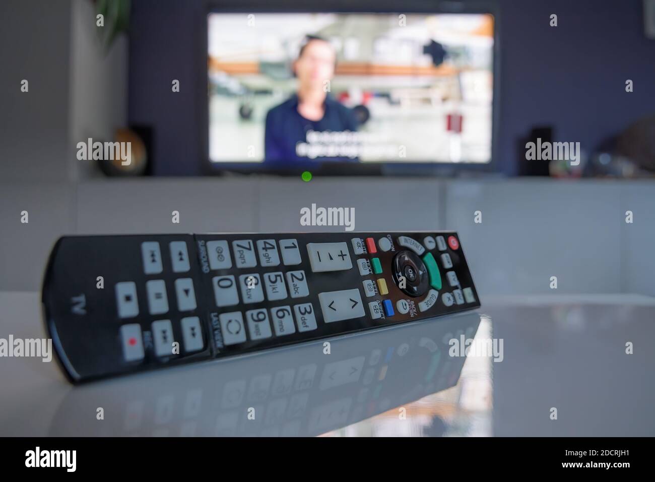 Close-up of TV remote controller on coffee table in front of smart television set. Television, technology, news and entertainment concepts Stock Photo