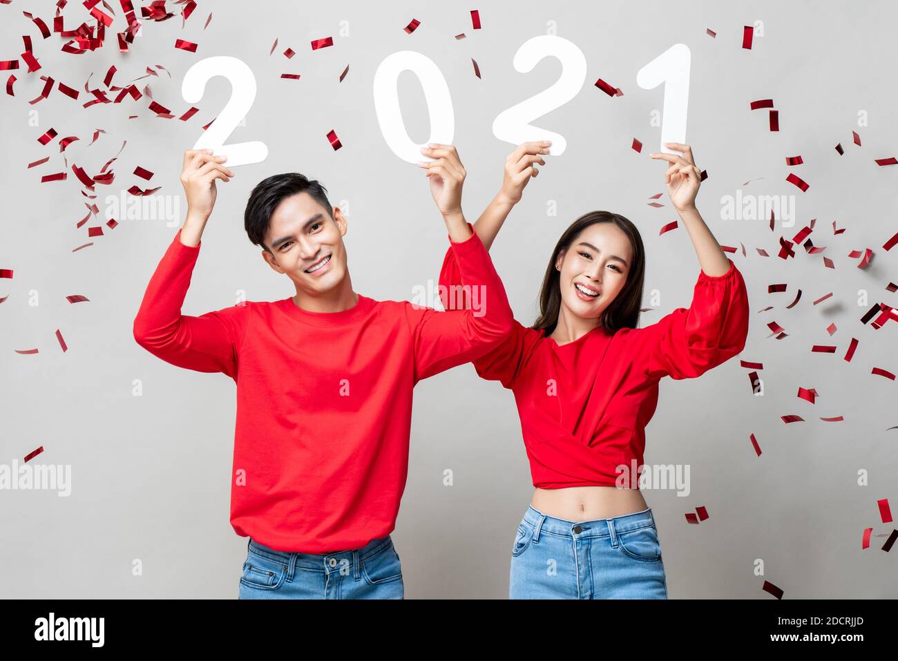 Smiling pretty Asian couple showing number 2021on light gray background with red confetti for new year concept Stock Photo