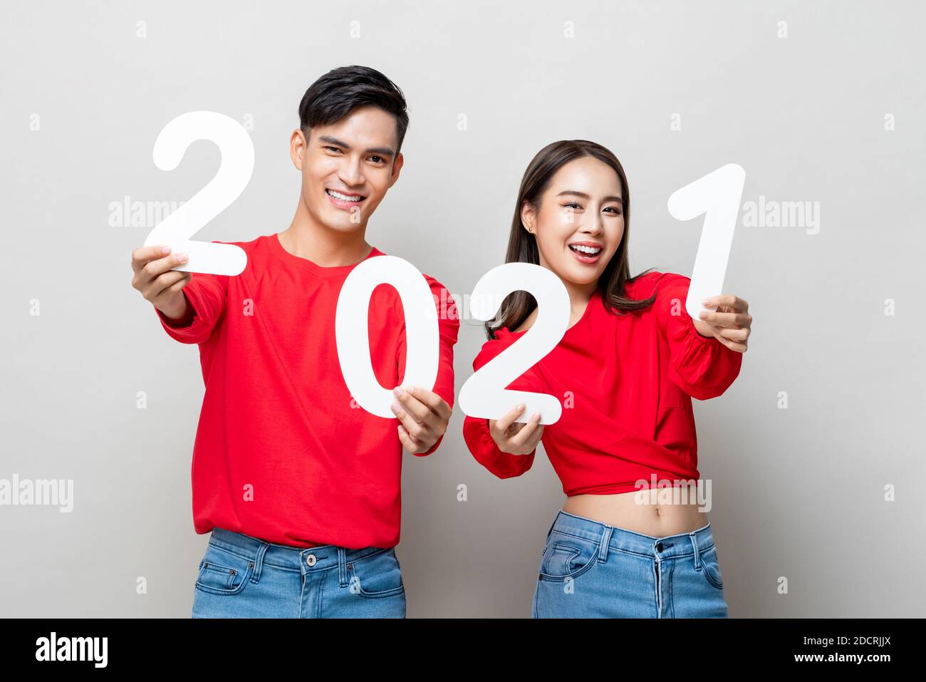 Happy Asian couple smiling and showing number 2021 for new year concept on light gray studio background Stock Photo