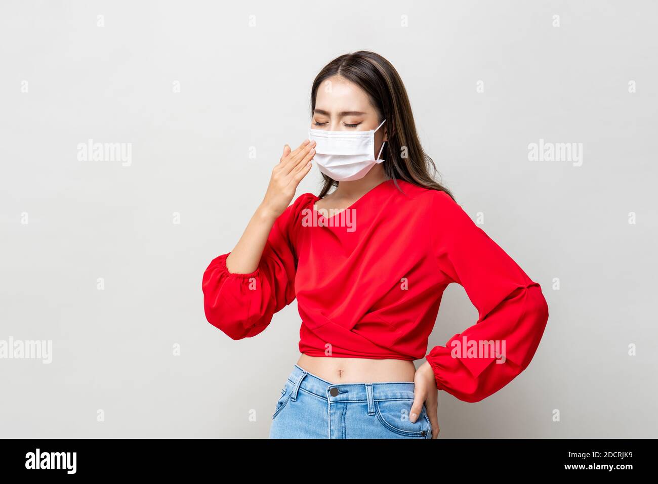 Asian woman wearing medical face mask coughing on light gray isolated background Stock Photo