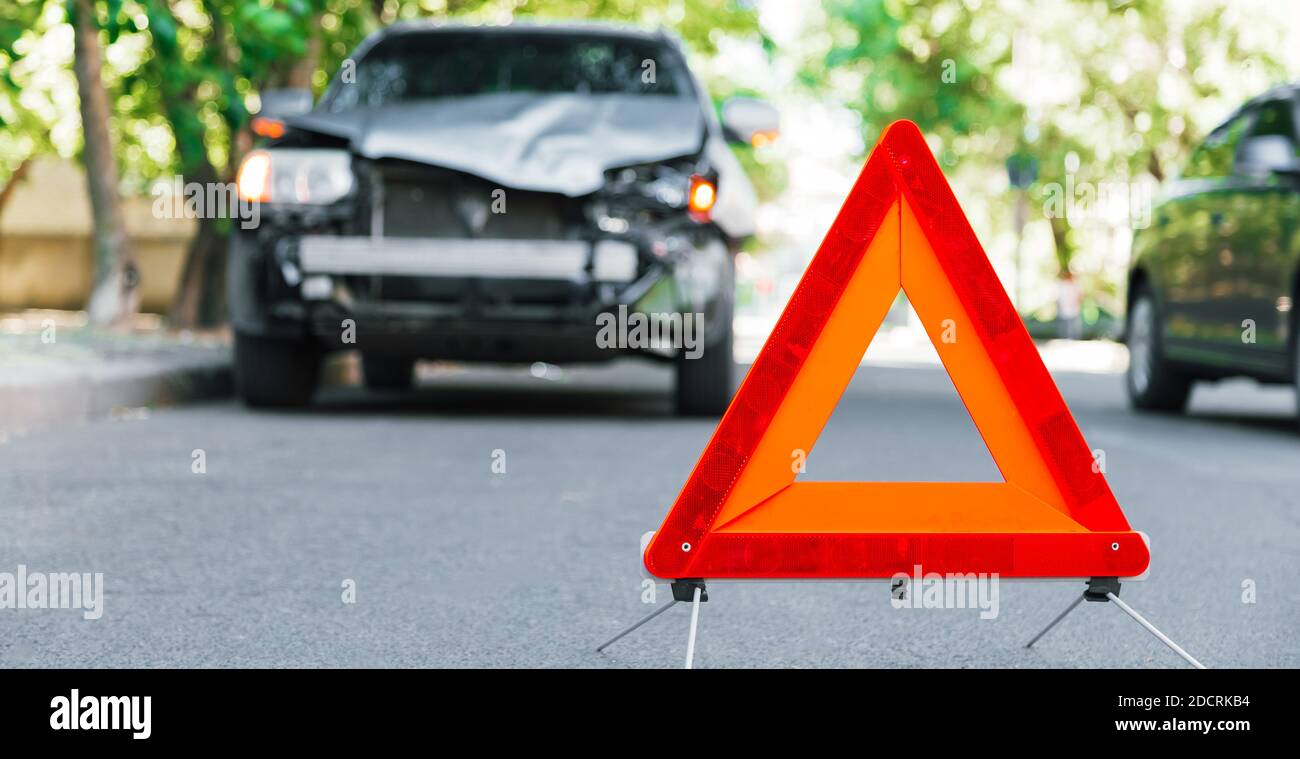 Red emergency stop triangle sign on road during a car accident. Broken gray car during road traffic accident. Car crash traffic accident on city road Stock Photo
