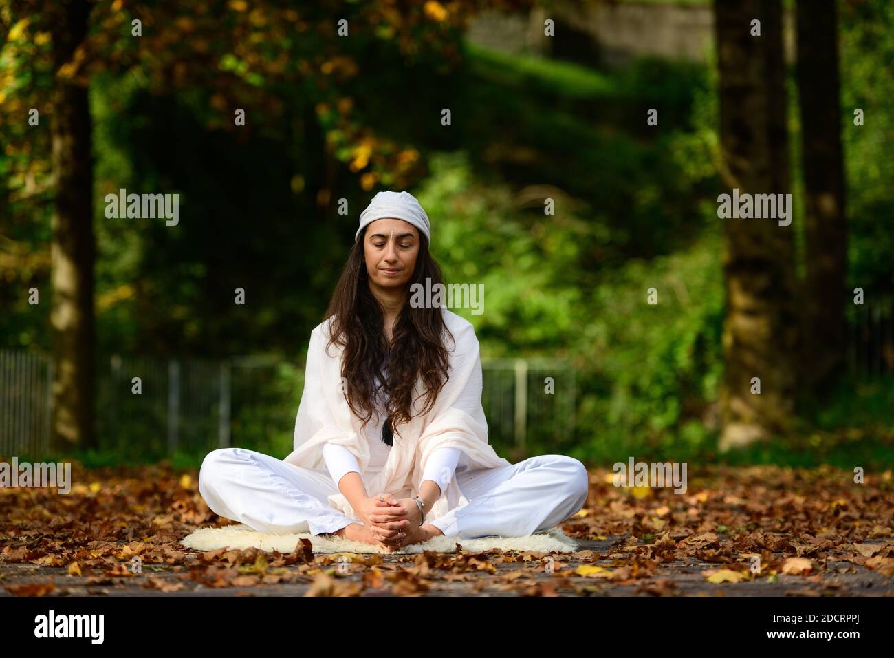 Woman in white in autumn park while doing yoga Stock Photo