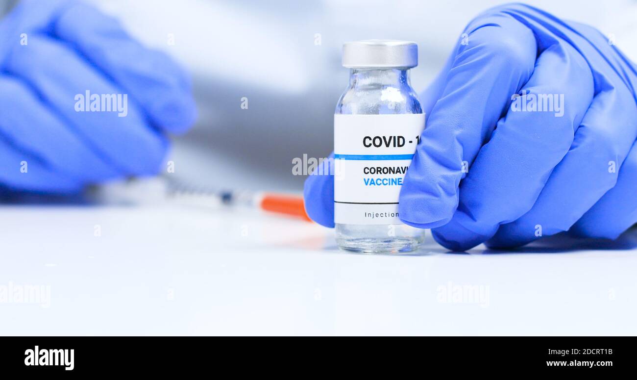 Corona virus Vaccine concept, doctor hands in blue medical gloves with transparent liquid coronavirus vaccine bottle and syringe for injection in the laboratory. Research and development of new cure for diseases Stock Photo