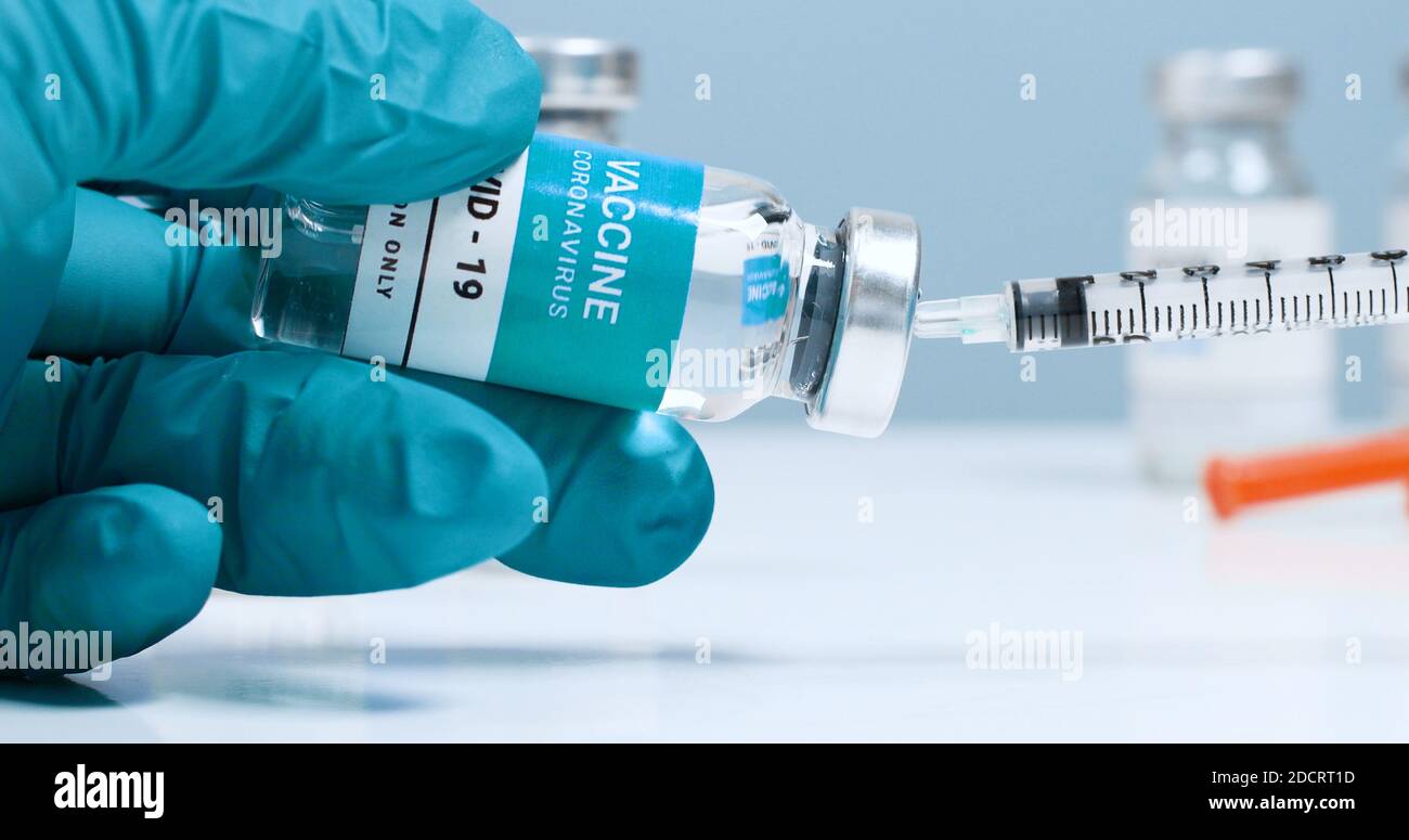 Female doctor hands in blue medical gloves with transparent liquid coronavirus vaccine bottle and syringe for injection in the laboratory. Research and development of new cure for diseases Stock Photo