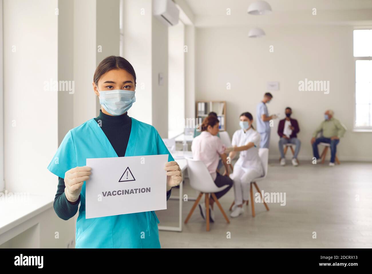 Young asian woman nurse in medical uniform and protective mask standing with sign vaccination Stock Photo