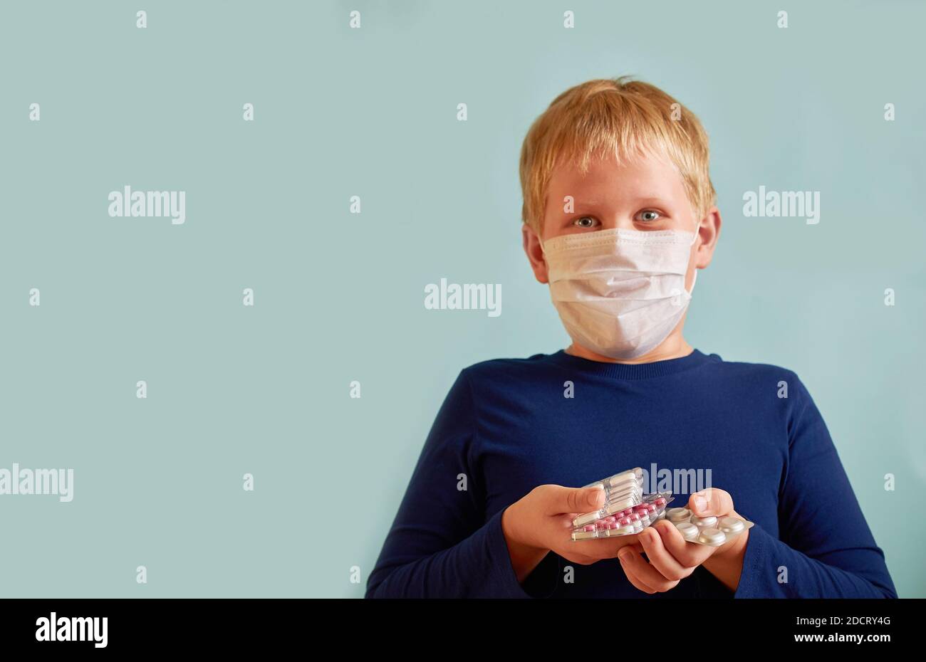 surprised European boy stands holding a pile of pills on a plain blue background Stock Photo