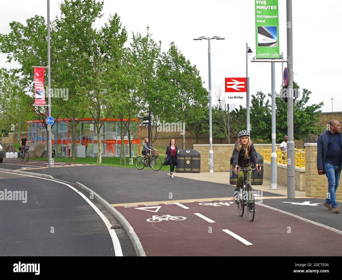 Cyclists use the new bike lane past Lea Bridge Station, London, UK. Part of Waltham Forest's Mini Holland scheme. Shows bike shelter beyond. Stock Photo