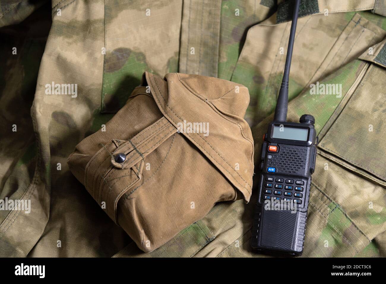 a black handheld radio lies next to the flask on a military camouflage jacket Stock Photo