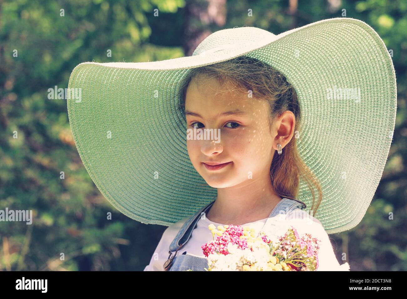 Cute smiling caucasian girl with flowers in a big hat on a summer background. Summer portrait Stock Photo