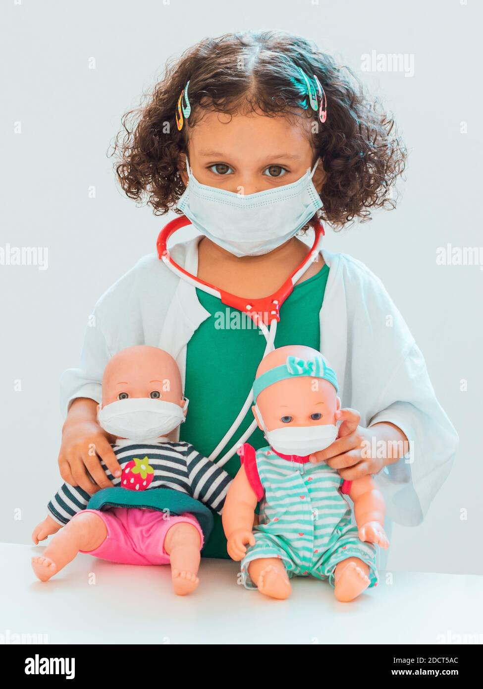 A girl who plays doctor with two baby dolls as a patient, they all wear protective masks Stock Photo