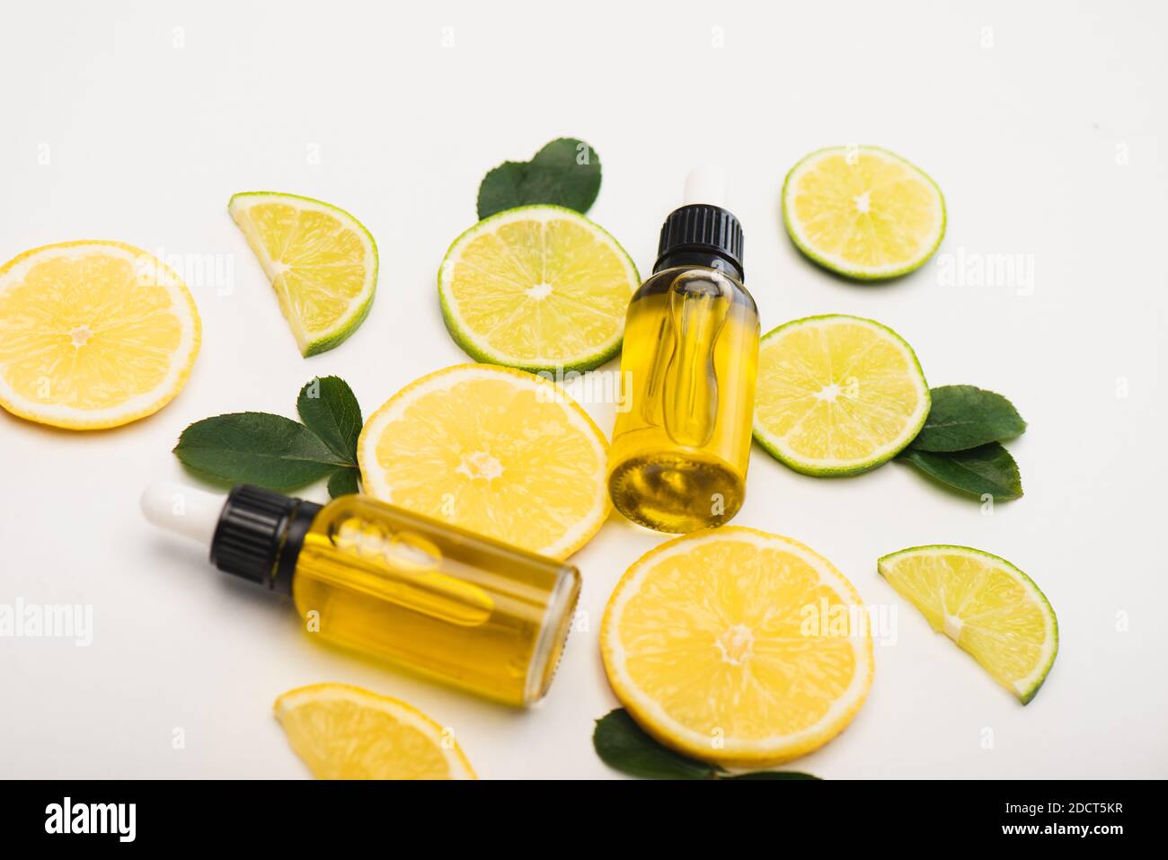 Bottles With Citrus Essence Fresh Lemon And Lime Slices Near Rose Leaves On White Surface Stock Photo Alamy