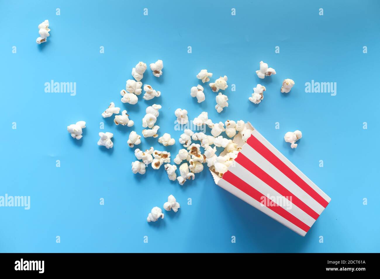 popcorn spilling from a container on blue background  Stock Photo