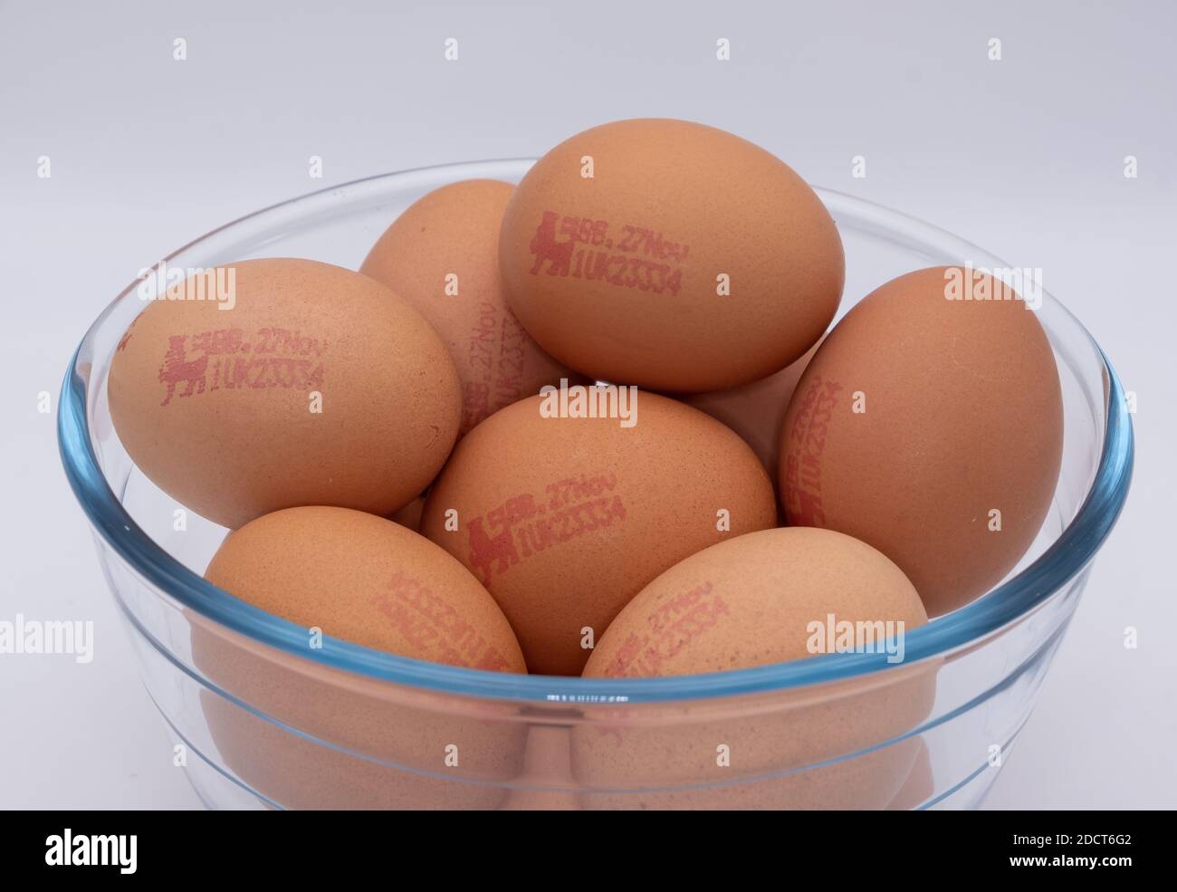 A dozen raw brown eggs with British Lion Mark in a glass bowl against a