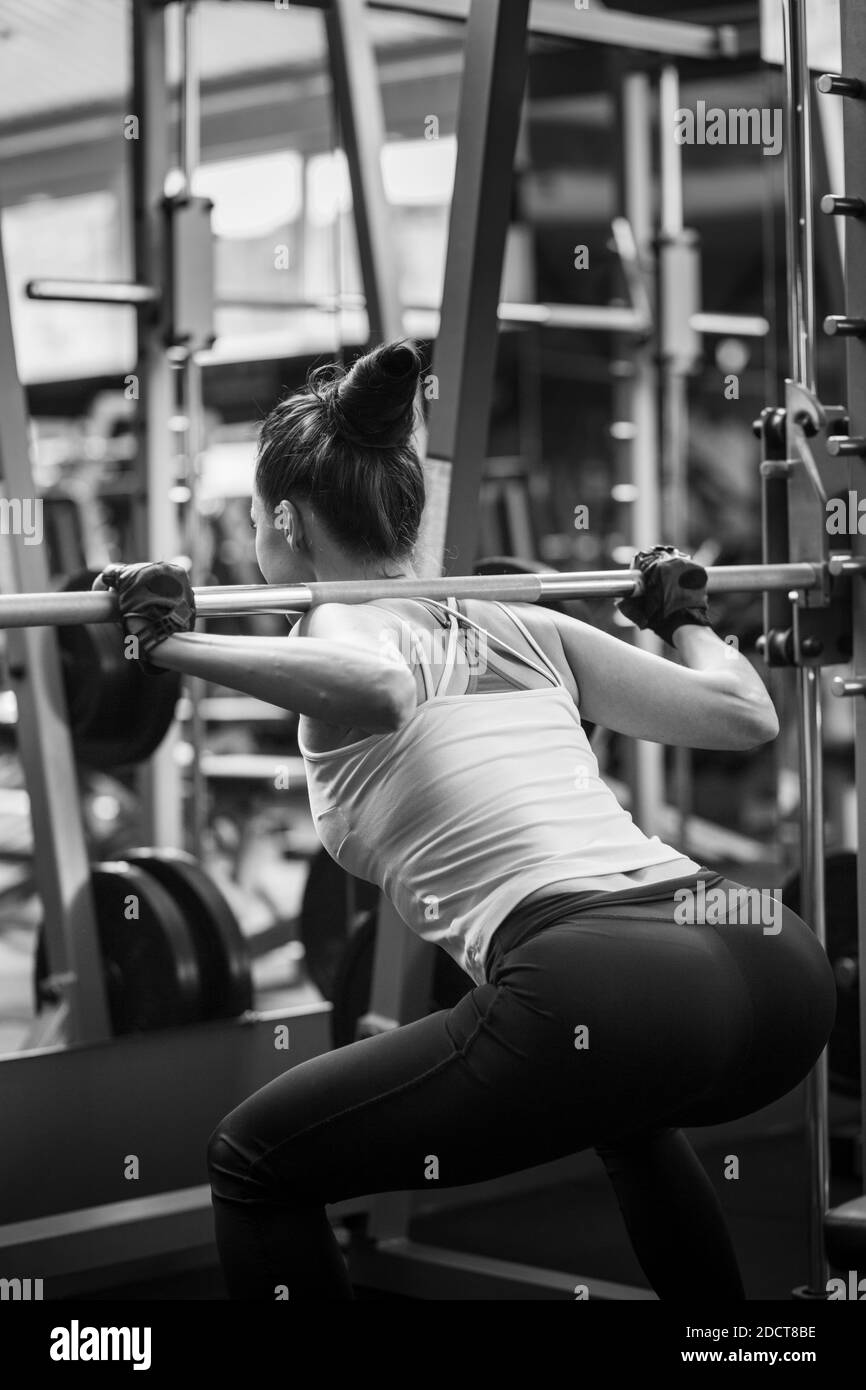 Young woman doing squats with barbell in gym Stock Photo