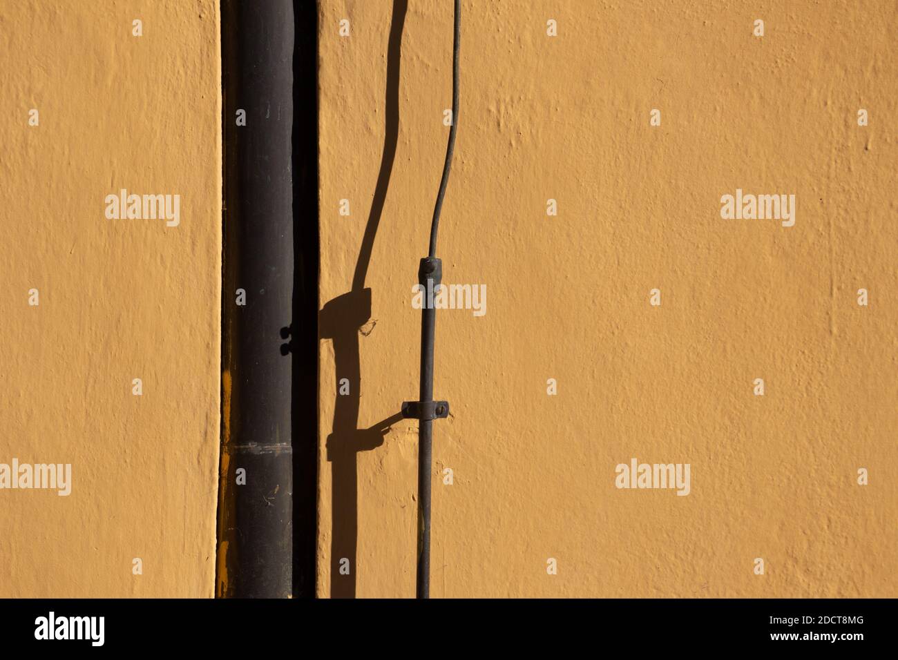 Brown metal downpipe and lightning rod casting shadows on a orange colored wall Stock Photo