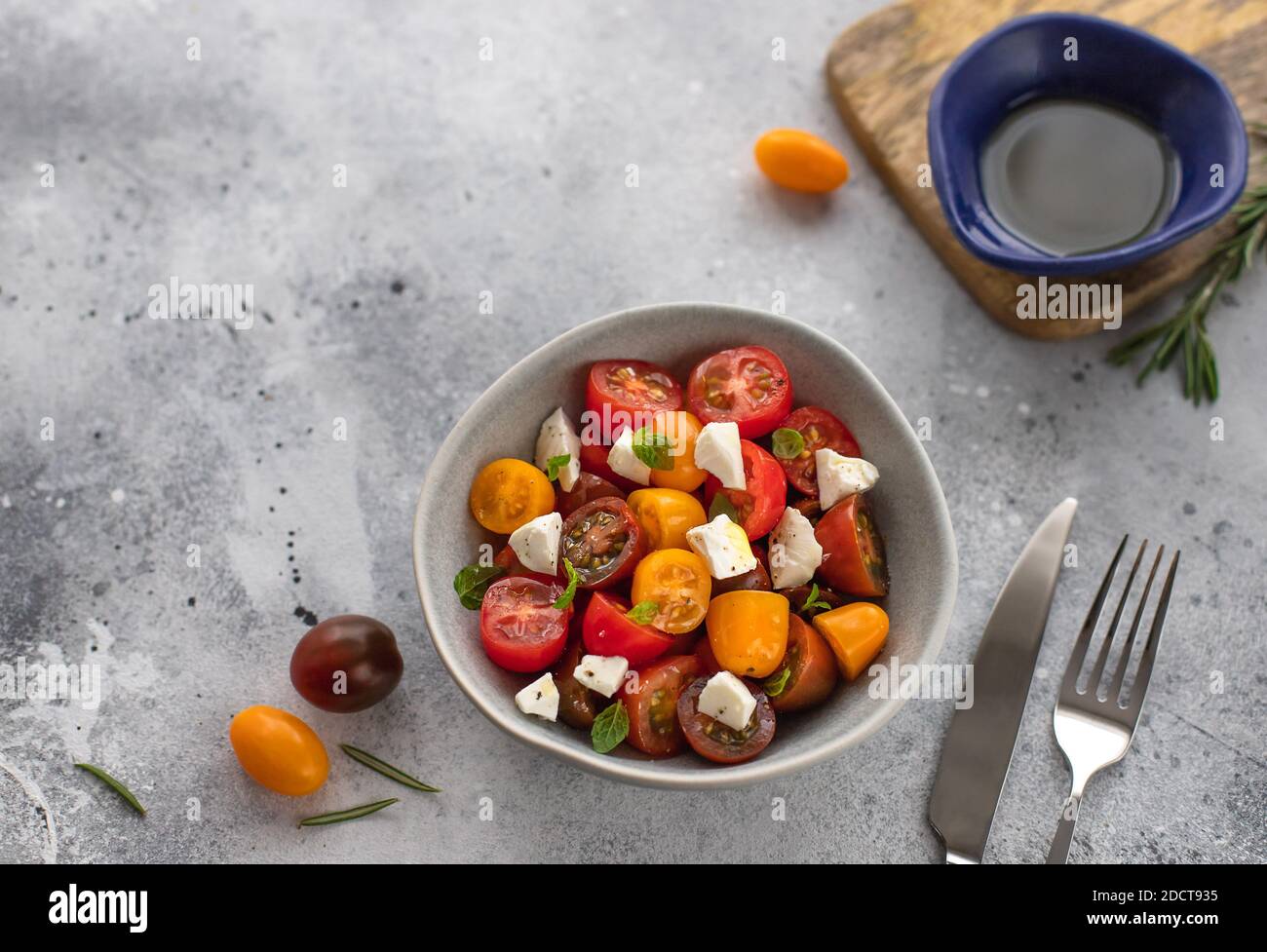Dietary salad with fresh cherry tomatoes, feta cheese, rosemary and olive oil. vegiterian healthy concept. gray concrete background, horizontal image Stock Photo