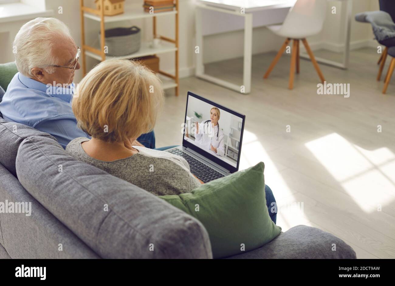 Older couple is sitting at home in the living room and talking to their family doctor via video link Stock Photo