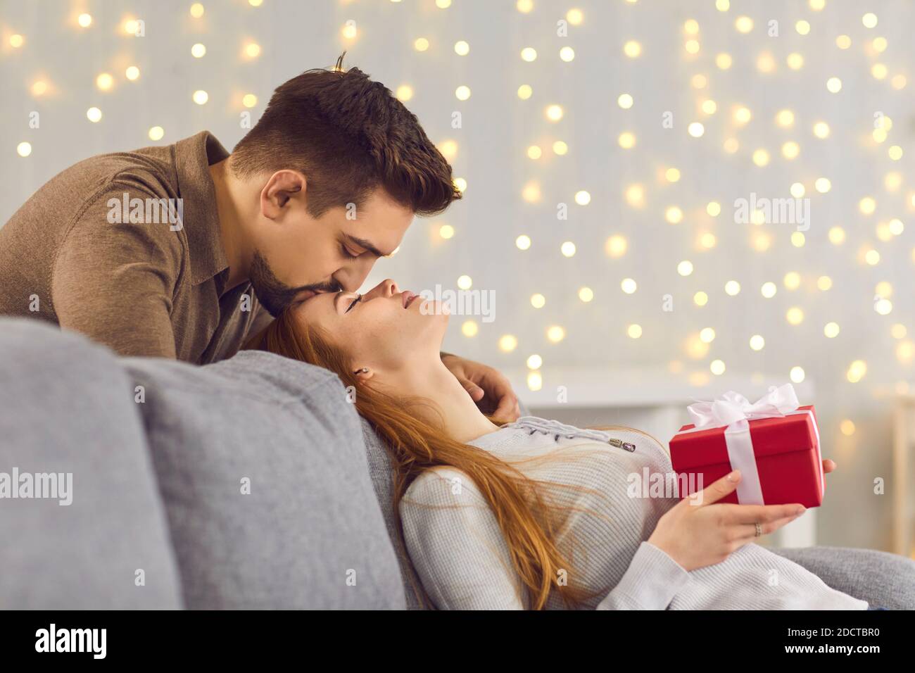 Side view of a loving husband kissing his young wife on the forehead after giving her a gift. Stock Photo