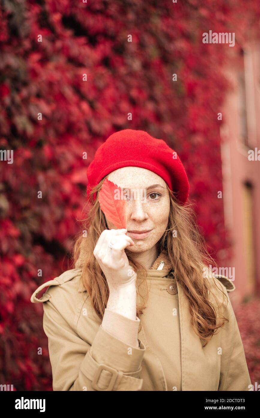 red-haired girl in a red beret and trench coat stands against the ...
