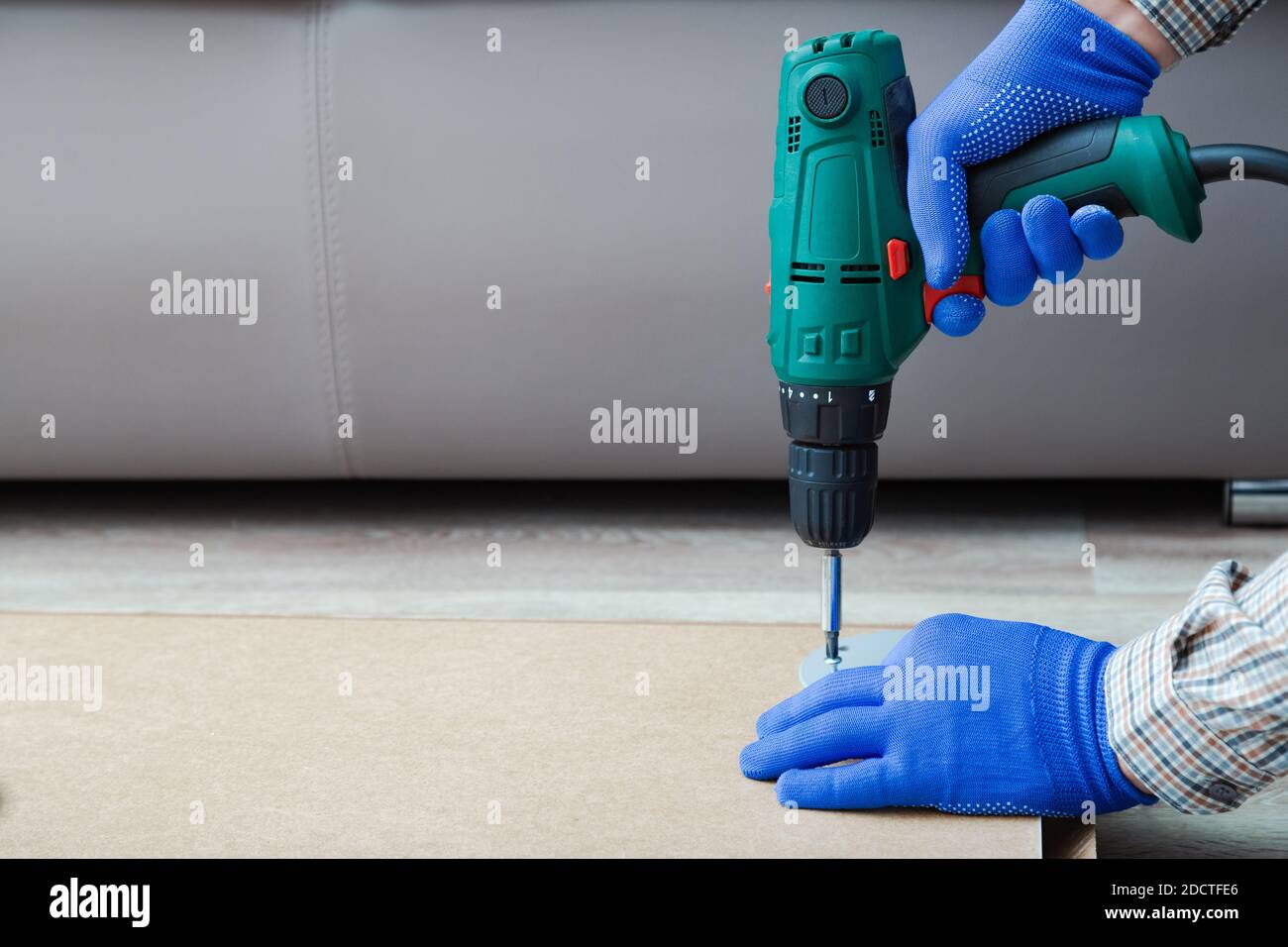 Electric Drill works in handyman hands. Male hands in gloves using electric drill tool to assemble and repair furniture at home. Copy space Stock Photo