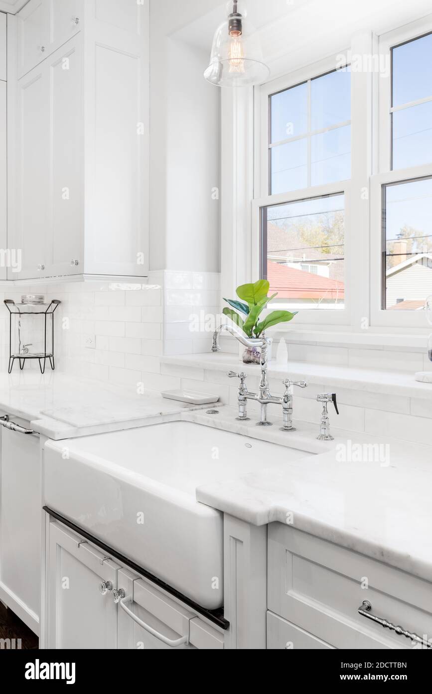 A luxurious, kitchen sink detail shot. The sink features a chrome faucet on a white apron sink in front of windows. Stock Photo
