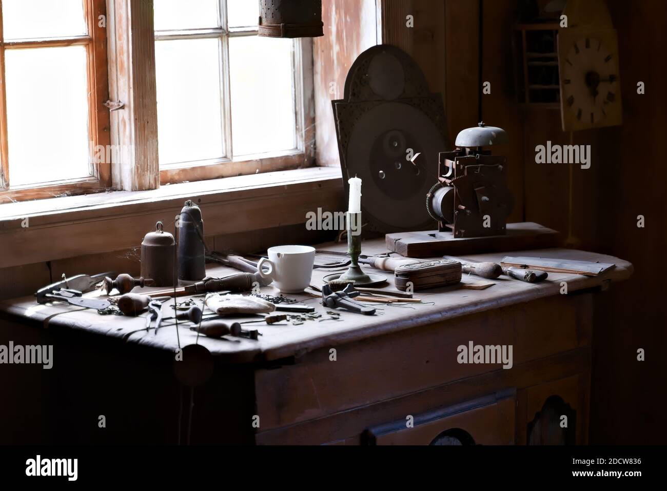Clockmakers workshop with tools and clock parts strewn on the table with natural sunlight streaming in through the window. Stock Photo
