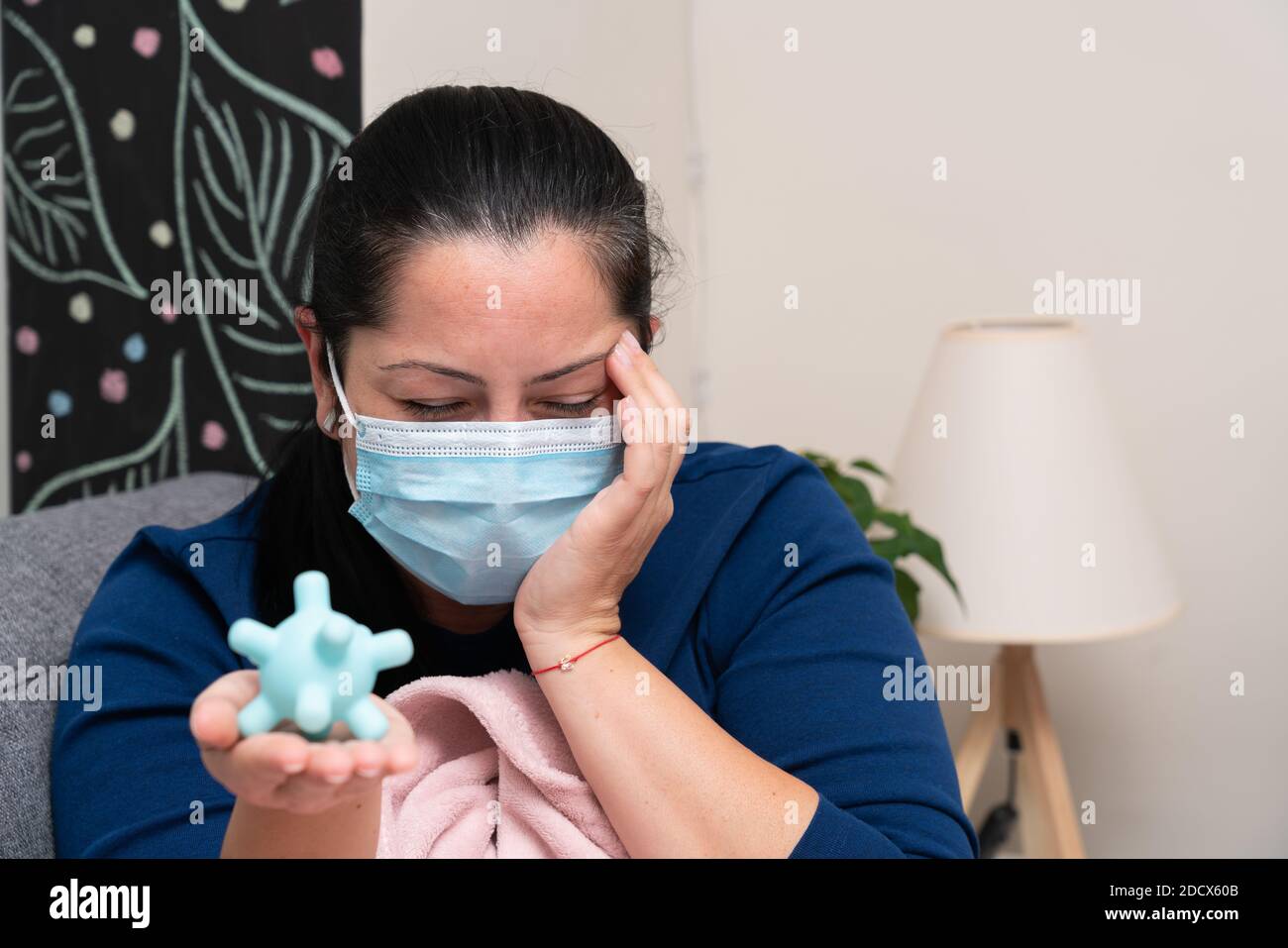Ill adult woman with concerned expression wearing medical or surgical mask to protect from covid19 influenza infection presenting fake virus as pandem Stock Photo