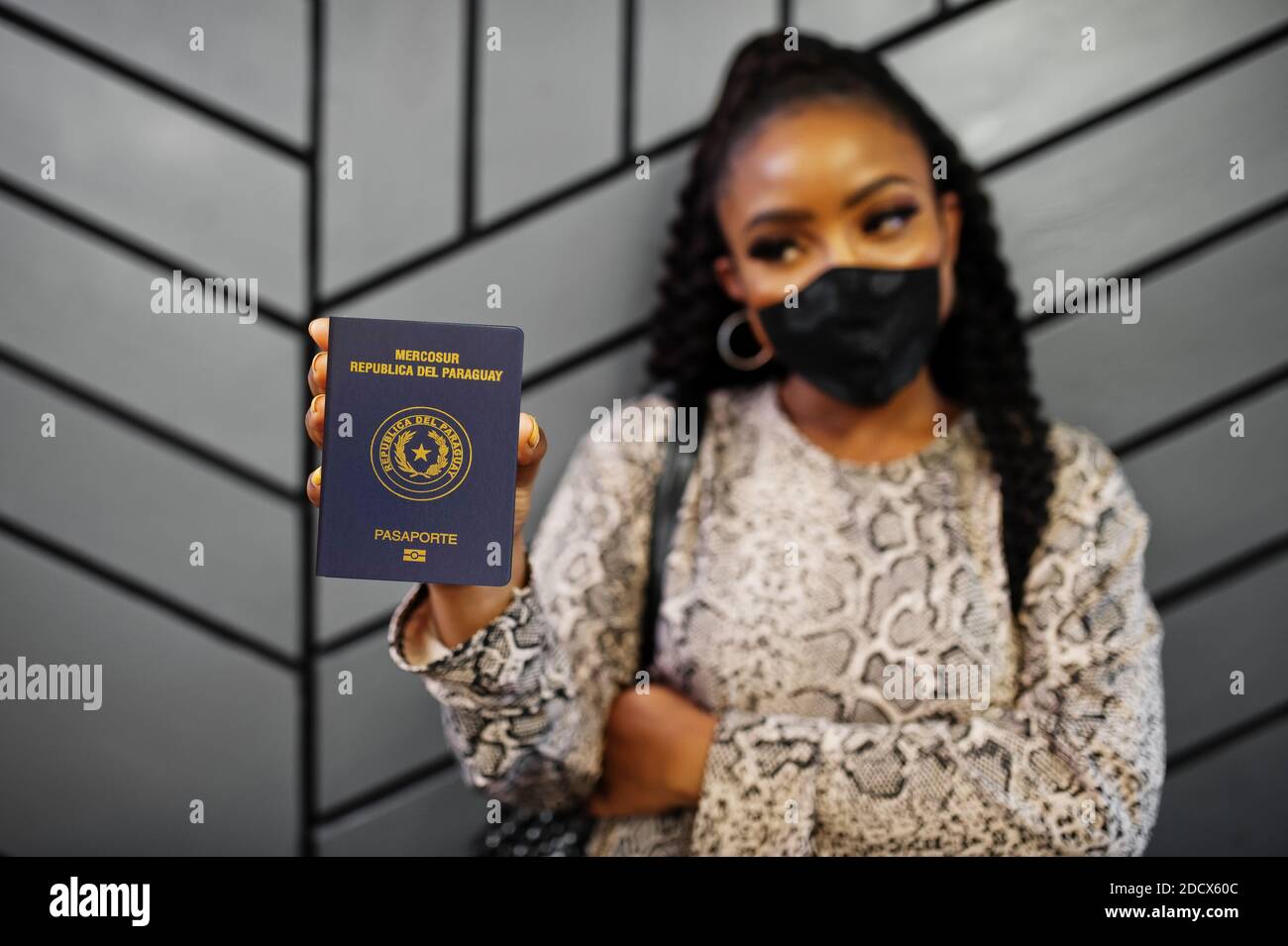 African american woman wearing black face mask show Paraguay passport in hand. Coronavirus in America country, border closure and quarantine, virus ou Stock Photo