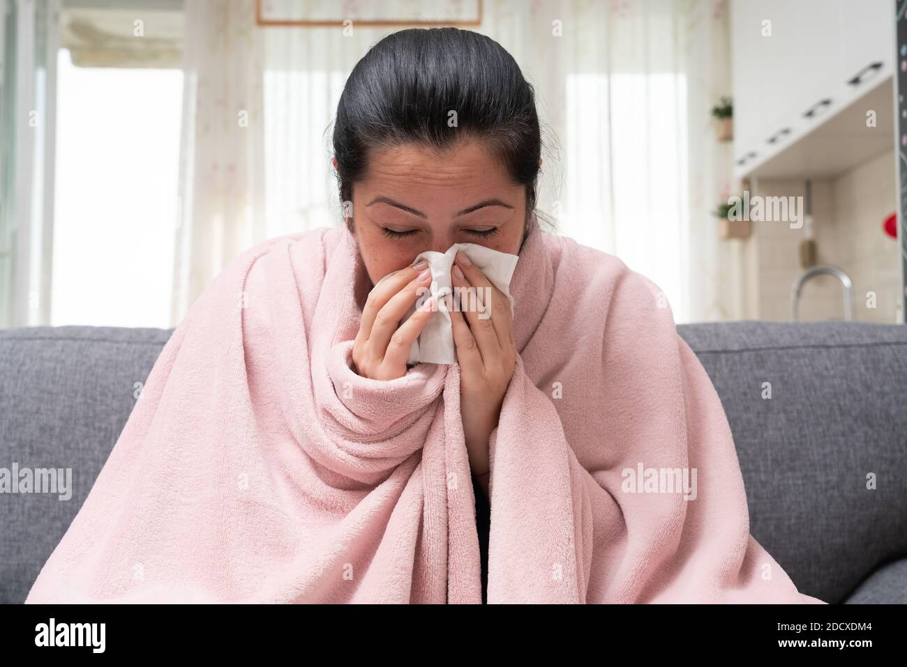 Sick adult female model on sofa blowing stuffy nose as sinusitis concept having sars covid flu influenza symptoms Stock Photo