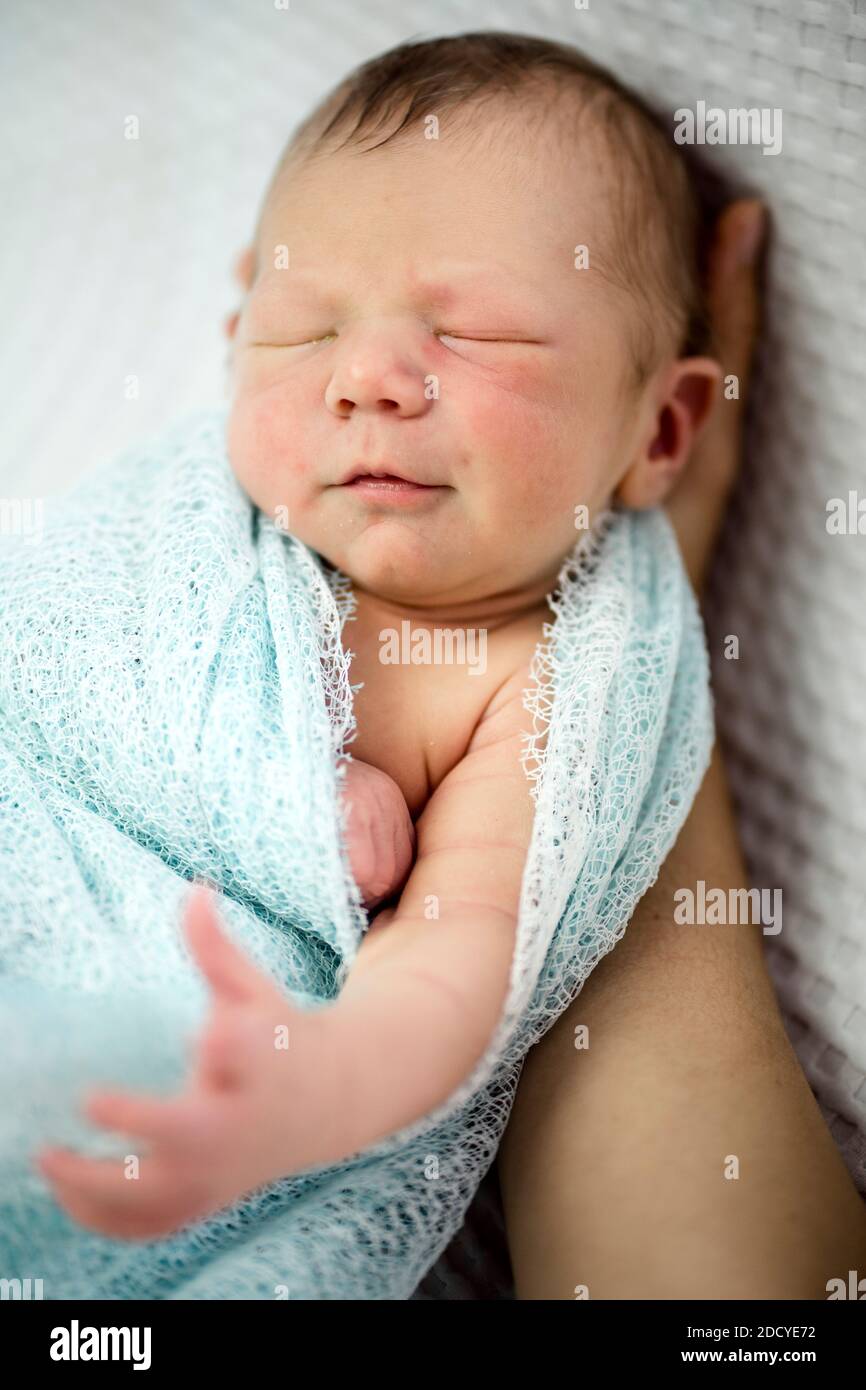 Cute sleeping newborn baby boy wrapped in blue laying on mother's hand