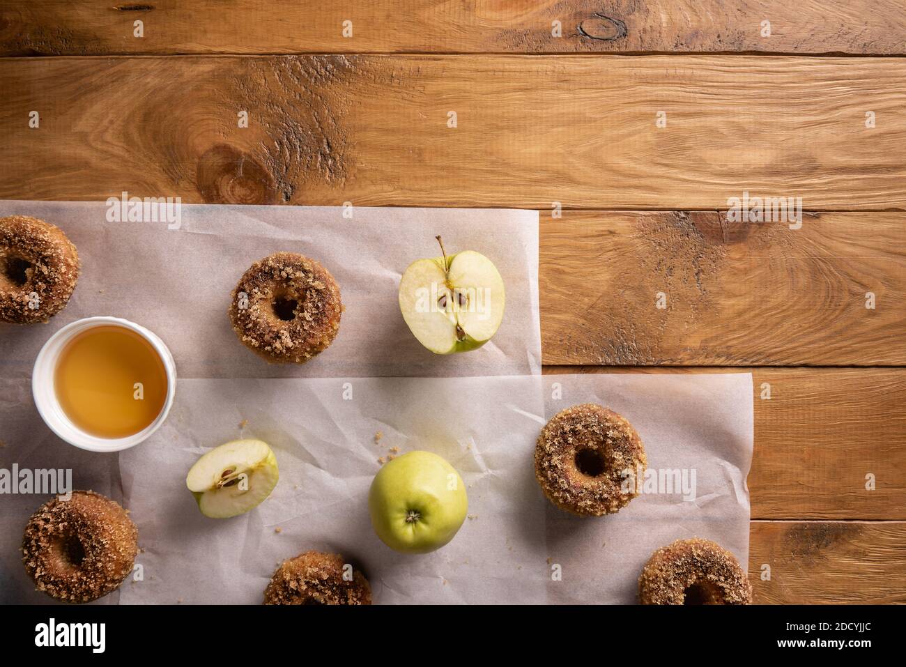 Baked apple cider donuts with apple fruits and cider on baking sheets on natural wooden table. Ready to eat snack. Small batch of homemade food. Direc Stock Photo
