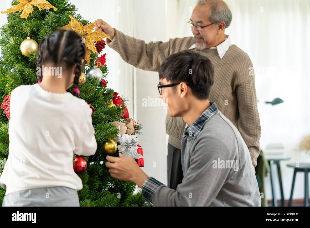 Multigenerational asian Family decorating a Christmas tree. Mom Dad daughter girl and grandfather decorate the Christmas tree prepare for season greet Stock Photo
