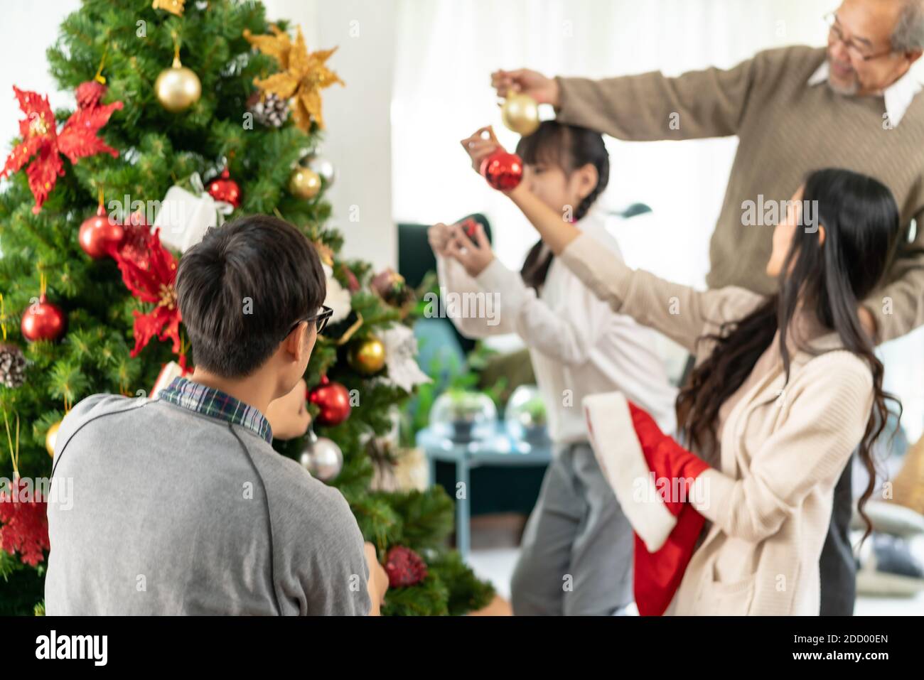 Multigenerational asian Family decorating a Christmas tree. Mom Dad daughter girl and grandfather decorate the Christmas tree prepare for season greet Stock Photo
