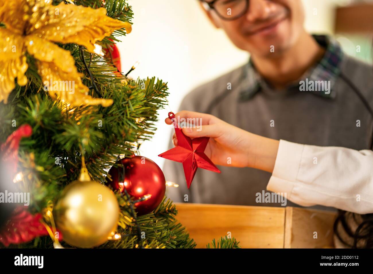 Close up hand little asian girl decorating a Christmas tree with ornament preparing for season greeting of Merry Christmas and Happy Holidays. Multige Stock Photo