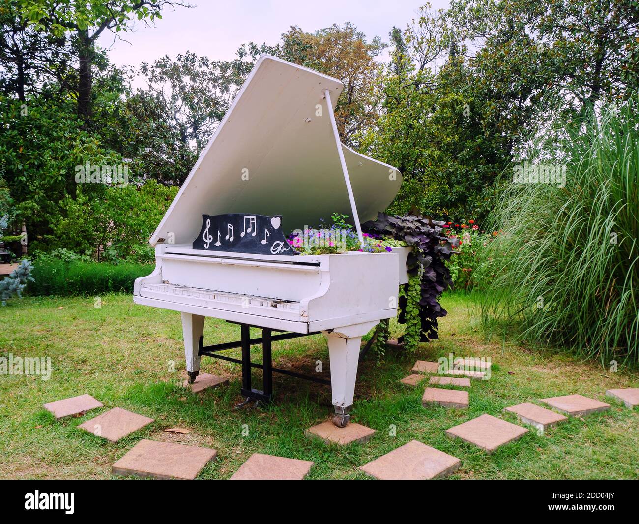 Decorative white grand piano decorated with flowers stands in the park ...