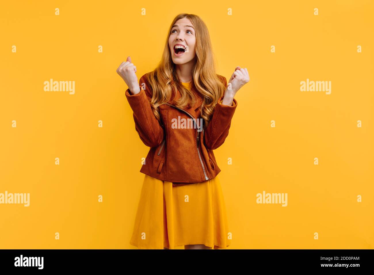 excited shocked screaming happy beautiful girl, in a bright yellow dress and autumn jacket, happily shows a winning gesture while standing on an isola Stock Photo