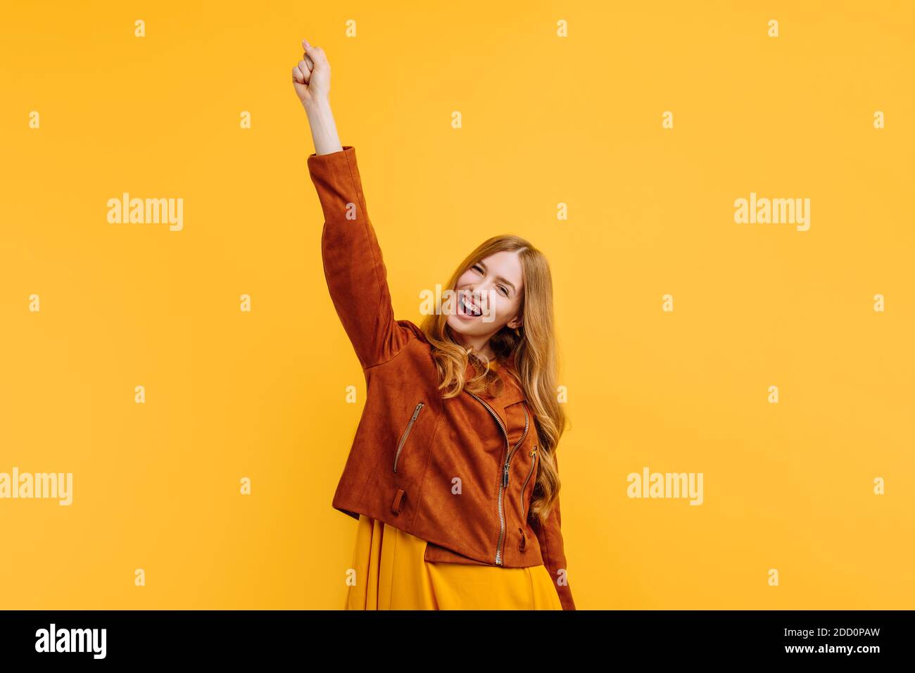excited shocked screaming happy beautiful girl, in a bright yellow dress and autumn jacket, happily shows a winning gesture while standing on an isola Stock Photo