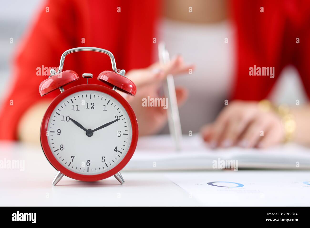 Against the background of businesswoman stands red alarm clock Stock Photo