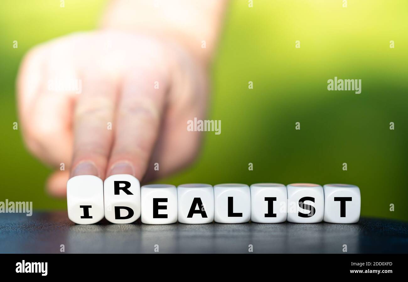 Hand turns dice and changes the word idealist to realist. Stock Photo