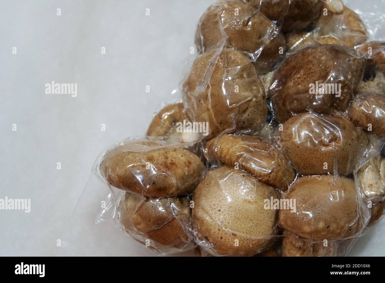 A vacuum package of raw brown shiitake mushrooms, on a white marble surface. Stock Photo